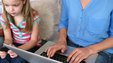 Mother-and-daughter-sitting-on-a-sofa-using-electronic-device