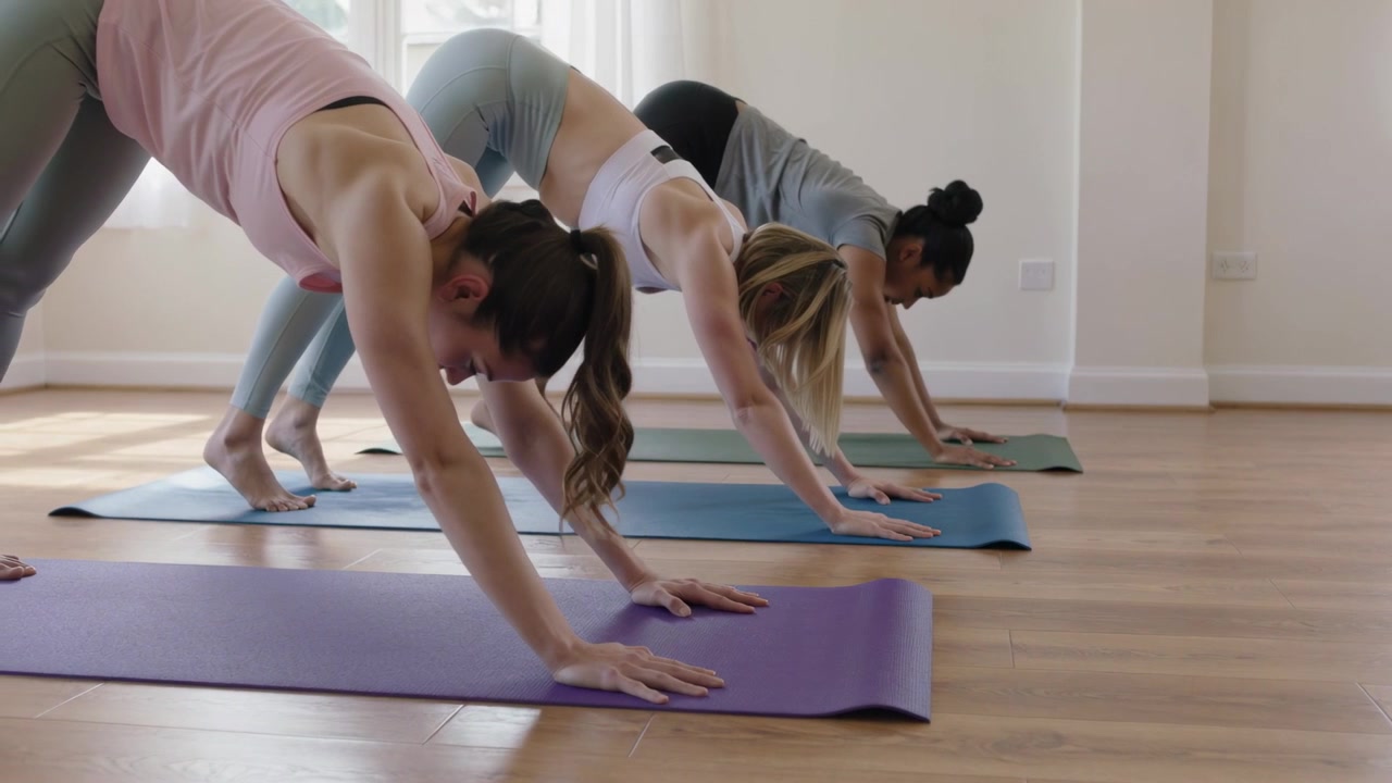 Tre donne che iniziano a perfezionare l'allineamento della posizione del cane a testa in giù in uno studio di yoga, sui tappetini, in leggings.