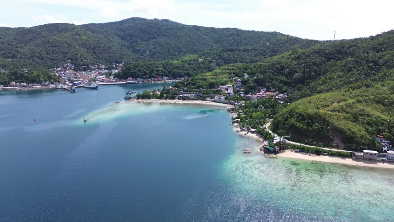 Vista aerea cinematografica della città e del porto di Romblon, nelle Filippine, che mostra la baia turchese, le case costiere, la spiaggia e le verdi colline sotto un cielo azzurro in una giornata tropicale e soleggiata, il tutto ripreso in 4K.