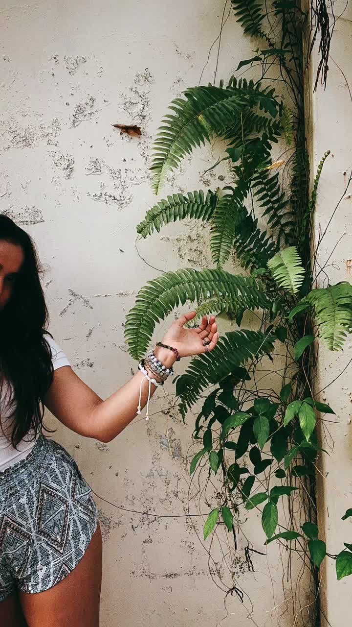 mujer de pie al lado de una planta de helecho exuberante en una pared