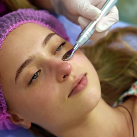 professional beautician conducts face procedures on girl`s face. the client lies on back. beautiful woman patient