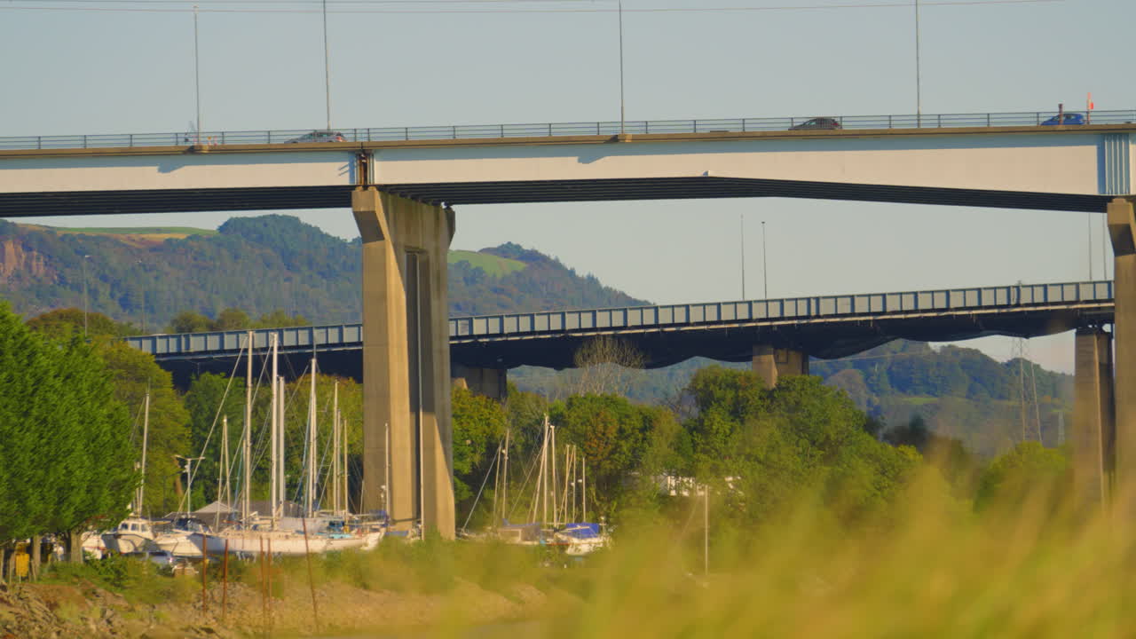 M4 Motorway Overpass Bridge with Cars Passing Commuting to Work Heading to Desination. Sailing Boats Docked Underneath with Hills in Background. 4K ProRes