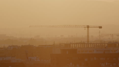 cityscape at sunrise/sunset with construction cranes and haze