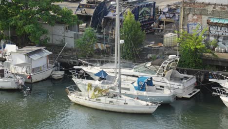 Aufgestapelte-Reihen-Angedockter-Segelboote-Schaukeln-Sanft-In-Den-Wellen-Des-Grünen-Kanalflusses