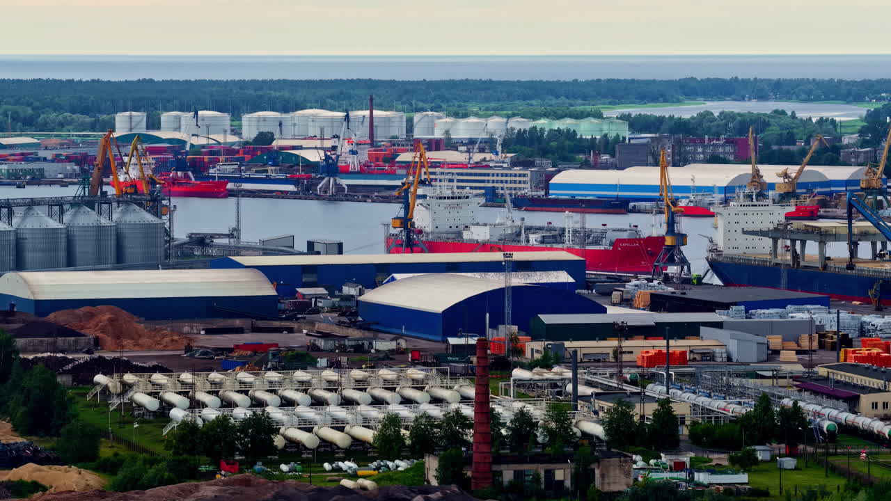 Extensive cargo port in Riga with cranes, storage tanks, silos, ships, and industrial facilities