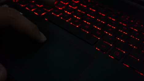 primer plano de un dedo que se mueve en el puntero del portátil con el fondo de la luz del teclado
