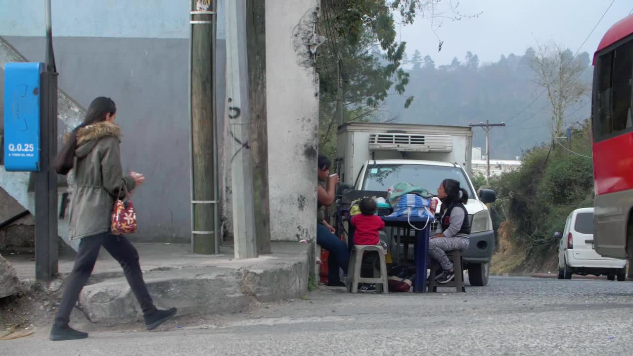Slow motion street view woman walking, family with kids at table, vehicles passing Zone 18 Guatemala City