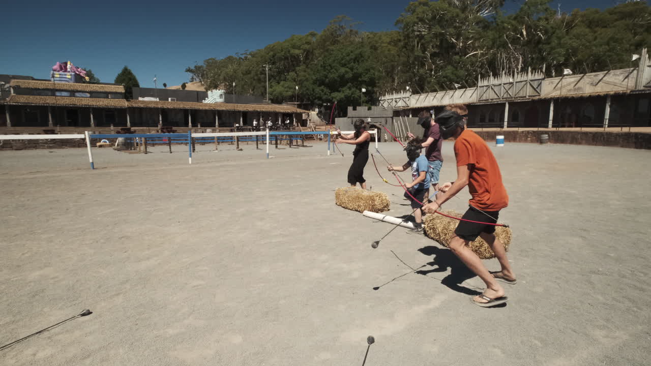 Young man with face guard shooting with bow and arrow against opponent during sunny day outdoors. Slow motion track shot.