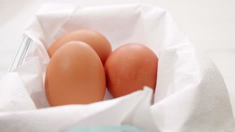 Close-up-of-three-organic-fresh-eggs-in-a-rotating-container-on-white-wrapping-paper-for-making-food