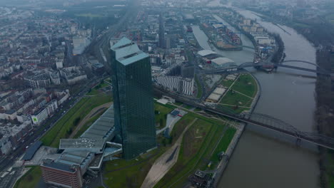 Erhöhter-Schuss-Des-Futuristischen-Wolkenkratzers-Der-Europäischen-Zentralbank.-Brücke-über-Den-Fluss-In-Der-Stadt-Und-Hafen-Im-Hintergrund.-Frankfurt-Am-Main,-Deutschland