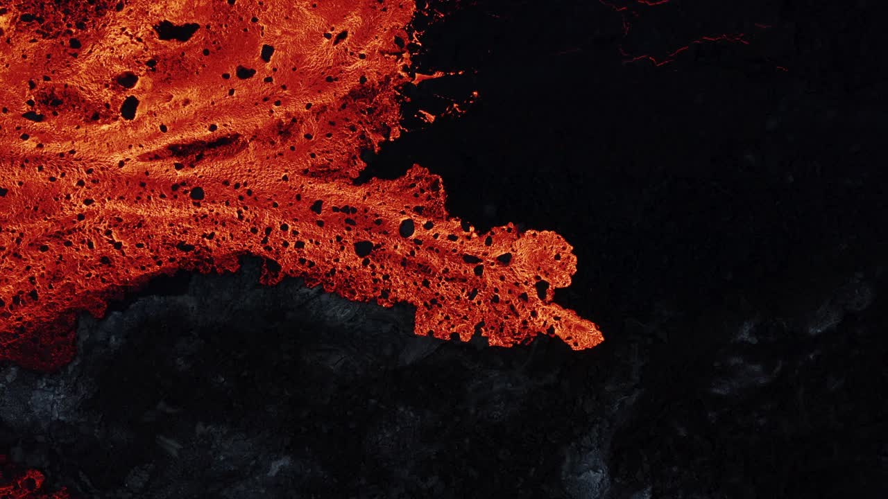 New molten lava river flowing slowly over dark basalt rock, top down