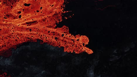 nuevo río de lava fundida que fluye lentamente sobre roca basáltica oscura, de arriba hacia abajo