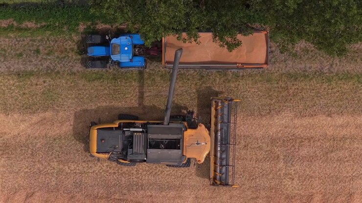 Combine harvester unloading grain into tractor trailer aerial top down view