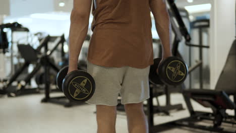 disparo de seguimiento de un hombre adulto en forma deportiva caminando en el gimnasio con pesas pesadas en las manos - vista posterior sin rostro