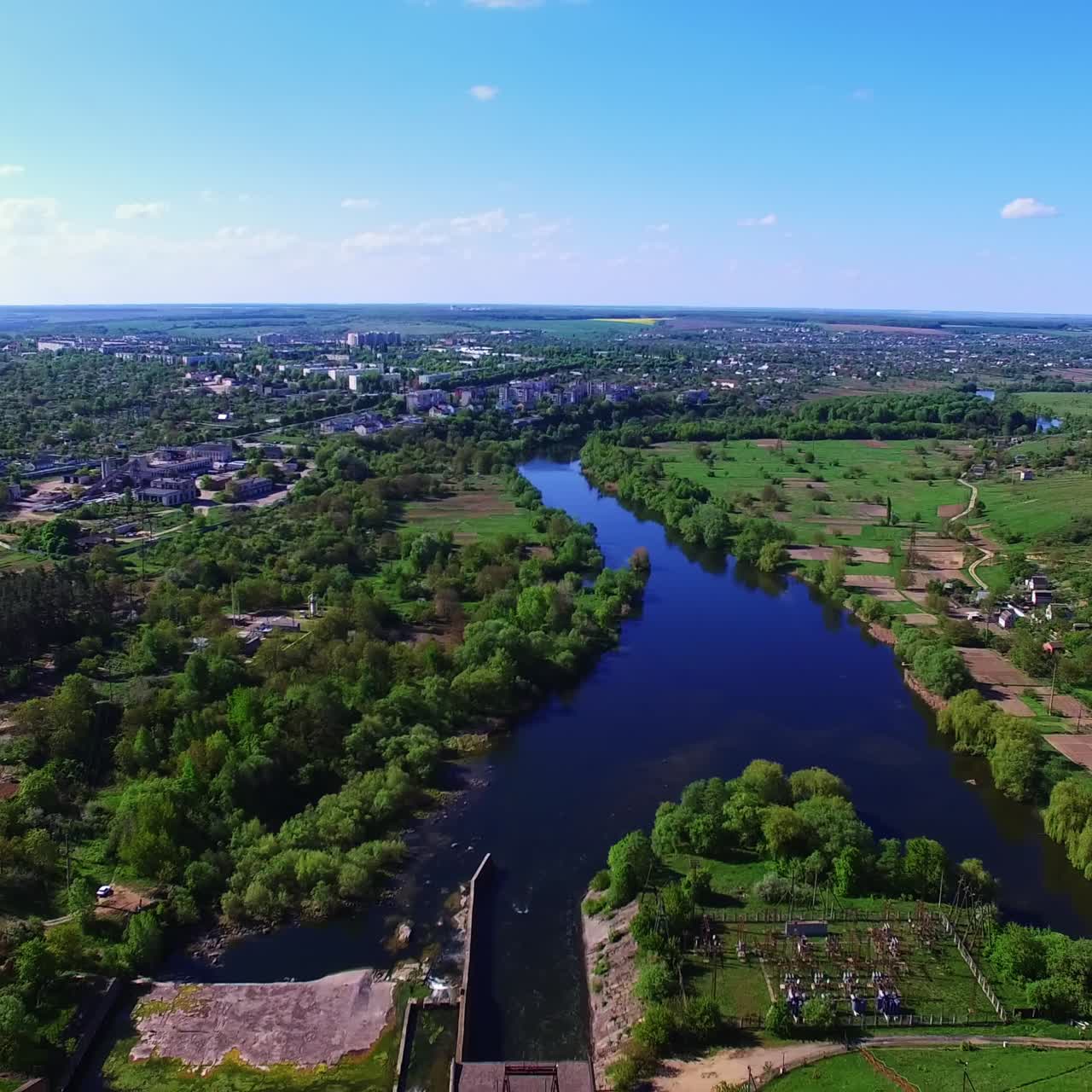 Blue river floating through the green city on sunny summer day. Urban landscape with water artery from aerial perspective