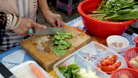 old hands chopping pak choi at open air kitchen, additional vegetables on table - medium shot, 25p