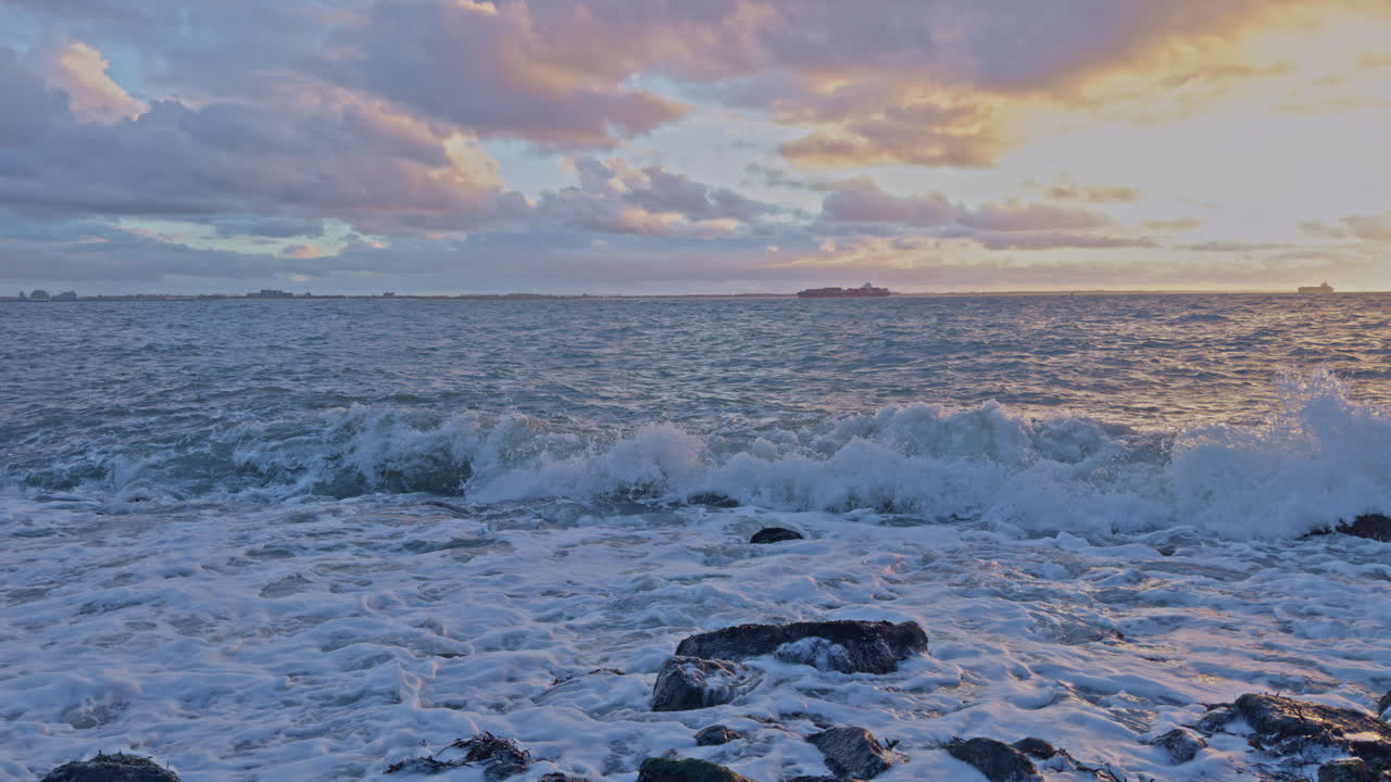Atlantic ocean sea shore waving scenery view of water waves with reefs, clouds, sunlight and sunset on the skyline horizon in the evening in North Europe, slow motion footage