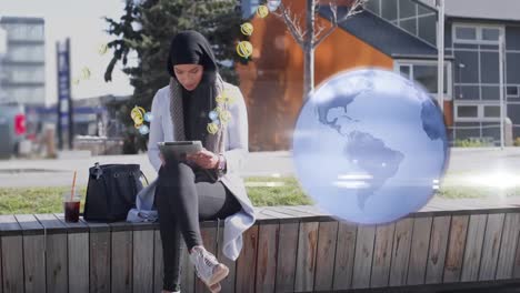 globo y múltiples iconos digitales flotando sobre una mujer en hijab usando una tableta digital en la calle