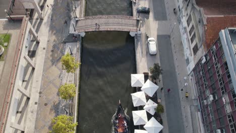 Aveiro-city-water-canal-with-canoe-and-building-rooftops,-aerial-top-down-view