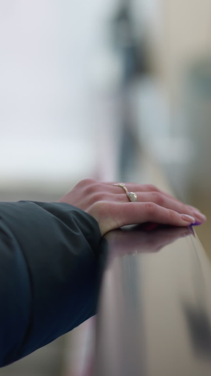 블랙 후디를 입은 손이 움직이는 에스컬레이터 레일에 누워있는 클로즈업, 반지로 장식, 배경은 손과 주변에 미묘한 초점을 맞추고 흐릿합니다.