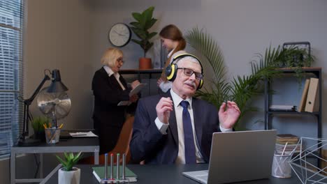 Happy-senior-business-man-entrepreneur-working-on-laptop-listening-music-on-headphones-and-dancing