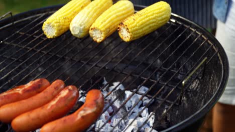 father and son grilling sausages and corns on barbecue