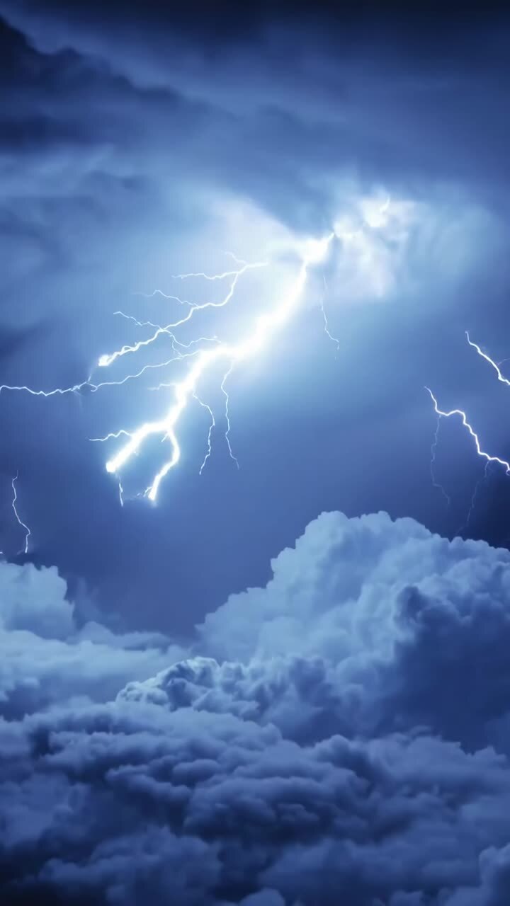 Video verticale: Campo di nuvole temporalesche che si illuminano per una scarica di notte, con fulmini ramificati.