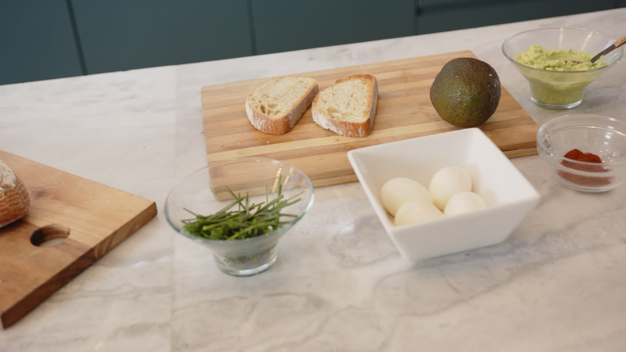 Preparing healthy meal, sliced bread, avocado, boiled eggs, and herbs on counter