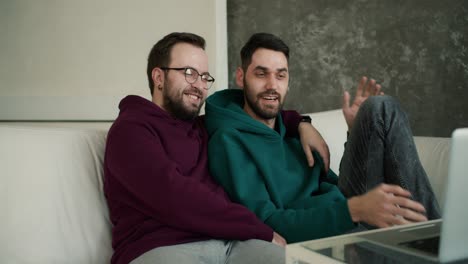 handsome gay couple using laptop, while sitting on a couch, watching movie and talk