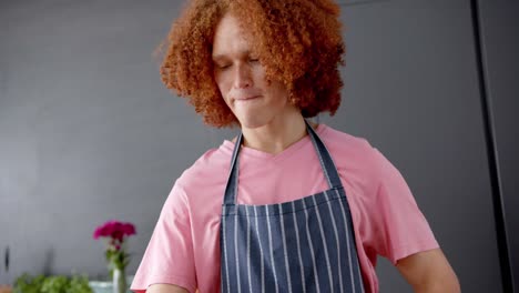 Biracial-man-with-curly-red-hair-wearing-apron-using-tablet-in-kitchen,-slow-motion