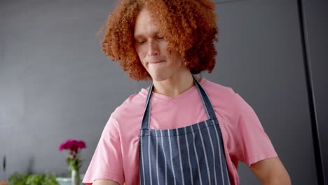 Hombre-Birracial-Con-Pelo-Rojo-Rizado-Usando-Delantal-Usando-Tableta-En-La-Cocina,-Cámara-Lenta