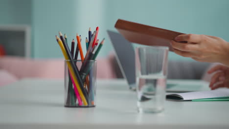 hand of woman taking book near colorful pencils in glass