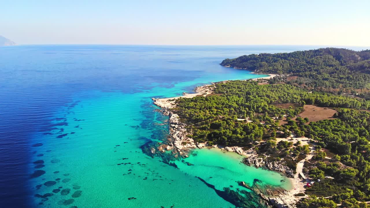Vista aerea da drone della costa rocciosa del Mar Egeo con acqua blu trasparente, vegetazione varia e colline. Grecia