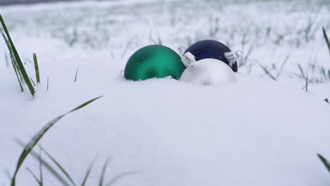 close up slow motion shot of multicolored christmas balls falling down and landing in soft snow outdoors during winter