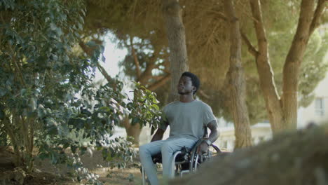 black man in wheelchair riding along park road on summer day