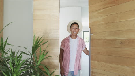 young asian man stands smiling at the entrance of a modern home