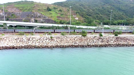 Hong-Kong-MTR-train-crossing-a-rural-part-of-Hong-Kong-bay,-Aerial-view