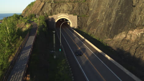 aerial, black mclaren luxury sports supercar driving out of tunnel during the day