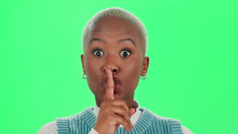 A woman in front of a green screen putting her finger to her lips in a 'shush' gesture