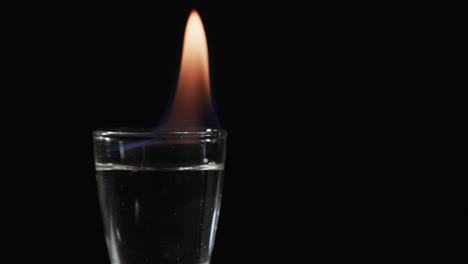 video of lit alcohol in glass with orange fire flame and copy space on black background