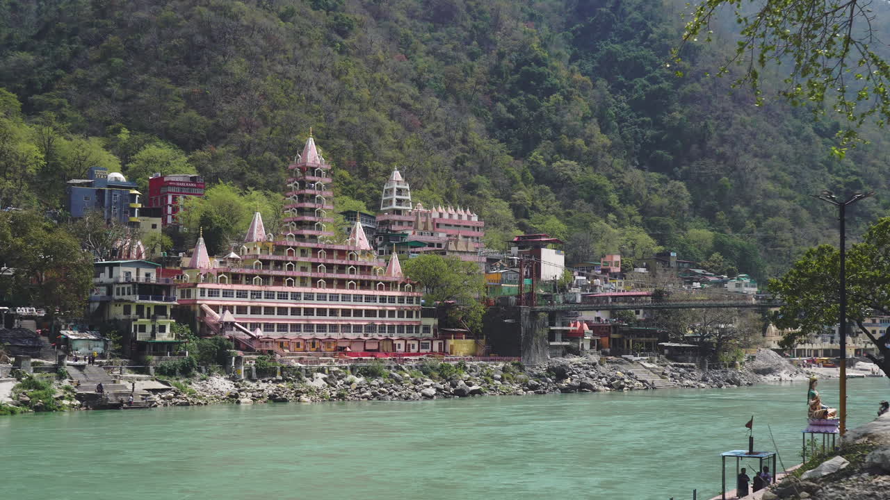 View of Rishikesh in Morning with Lakshman Jhula bridge in frame and raft with tourists on the ganga river.