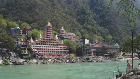 view of rishikesh in morning with lakshman jhula bridge in frame and raft with tourists on the ganga river.