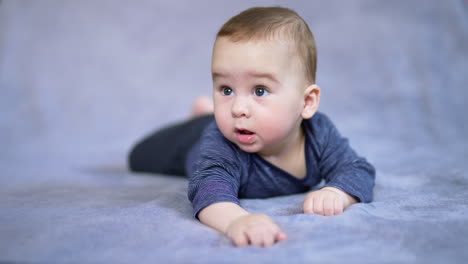 beautiful adorable baby boy lies on soft plaid. little kid looking at something with interest with open mouth. close up. grey backdrop in blur.