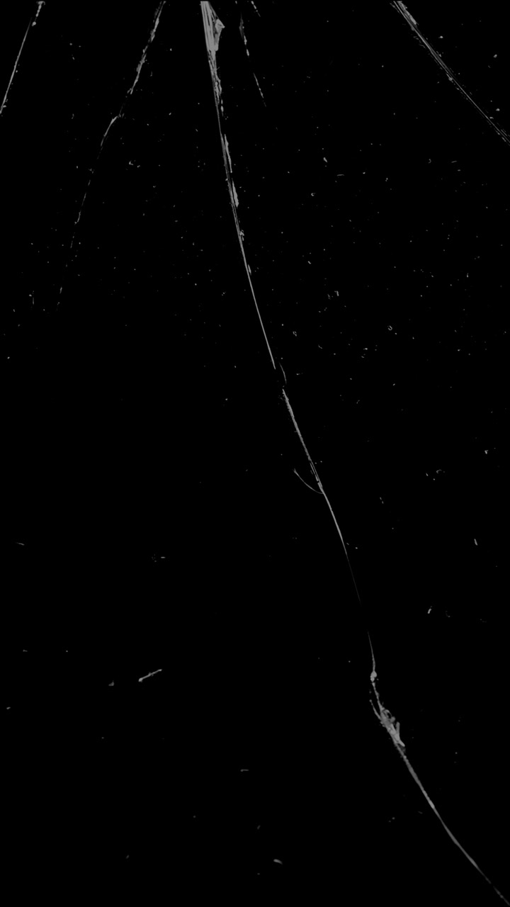 Una singola, lunga e sottile crepa percorre una superficie di vetro. Una sovrapposizione verticale minima per rappresentare danni lievi, stress o uno stato di frattura.