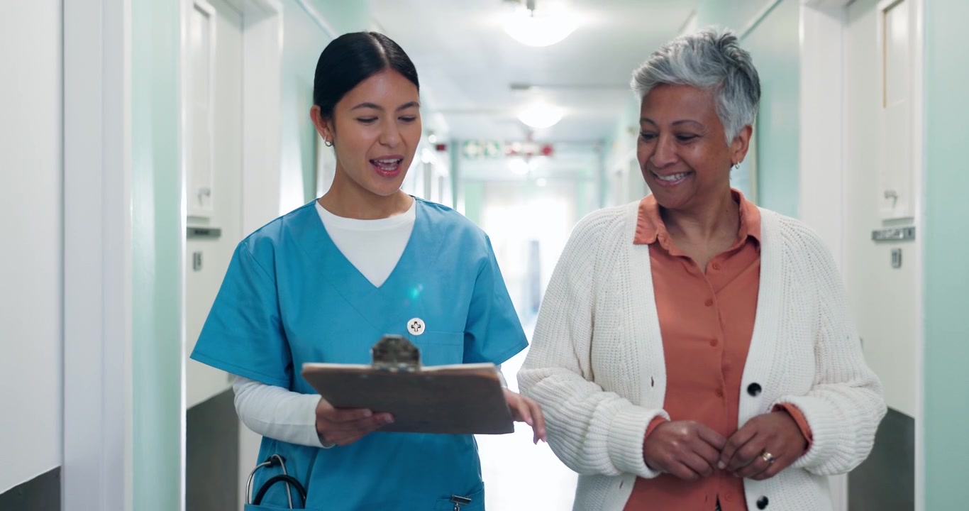 Nurse Talking to Senior Patient While Walking Down Hospital Hallway