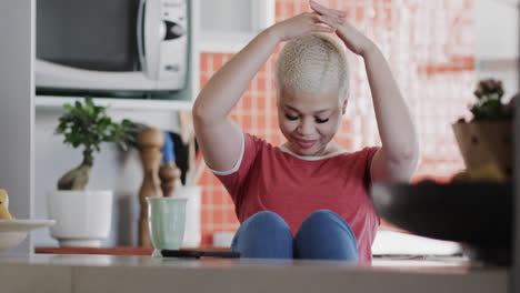 mujer biracial feliz con teléfono inteligente relajándose en casa en cámara lenta