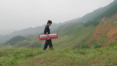 Pensive-male-walking-with-style-holding-a-piano-through-tropical-mountains-of-Southeast-Asia