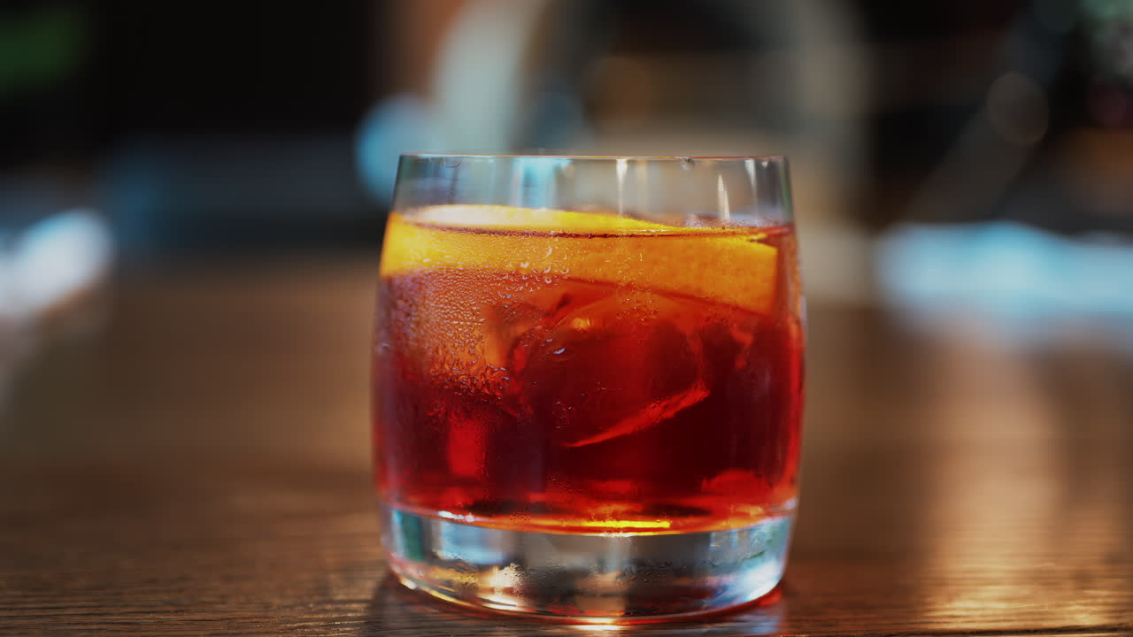 Close up of a Negroni cocktail with orange slice and ice cubes on a wooden table