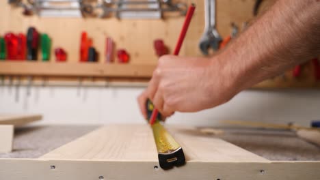 Close-up-caucasian-hand-measuring-and-marking-a-wooden-plate-with-a-pencil