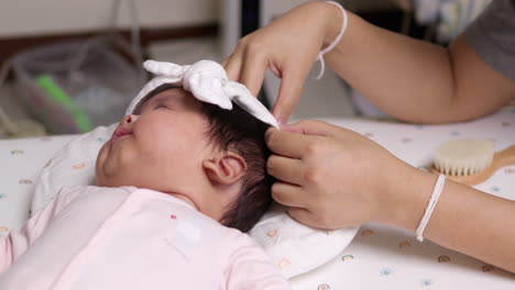 a mom is putting on a white headband on her newborn child's head while it is sleeping.